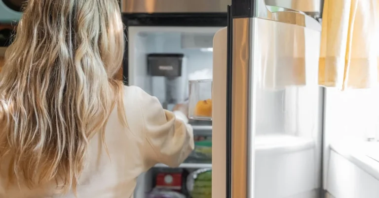 Otwarta lodówka z produktami na półkach, osoba wyjmująca jedzenie