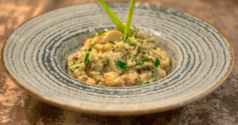 Risotto z parmezanem rozlane falą na płaskim talerzu, kremowe ziarna ryżu