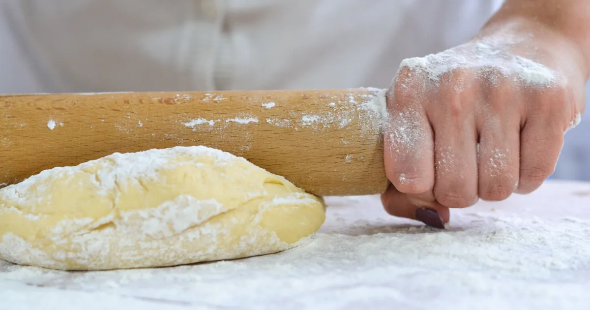 Ciasto na pierogi wałkowane drewnianym wałkiem na blacie oprószonym mąką