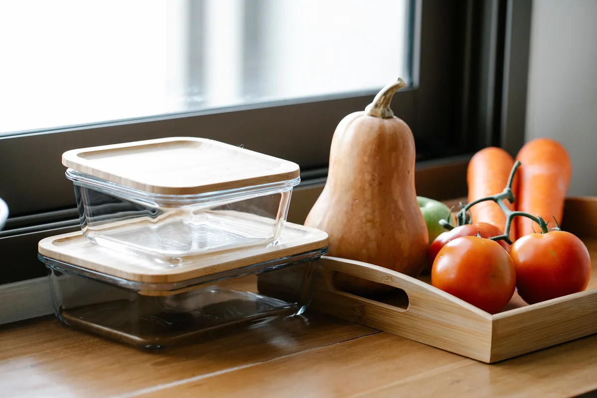 Szklane pojemniki z pokrywkami do meal prep na kuchennym blacie, obok dynia i pomidory