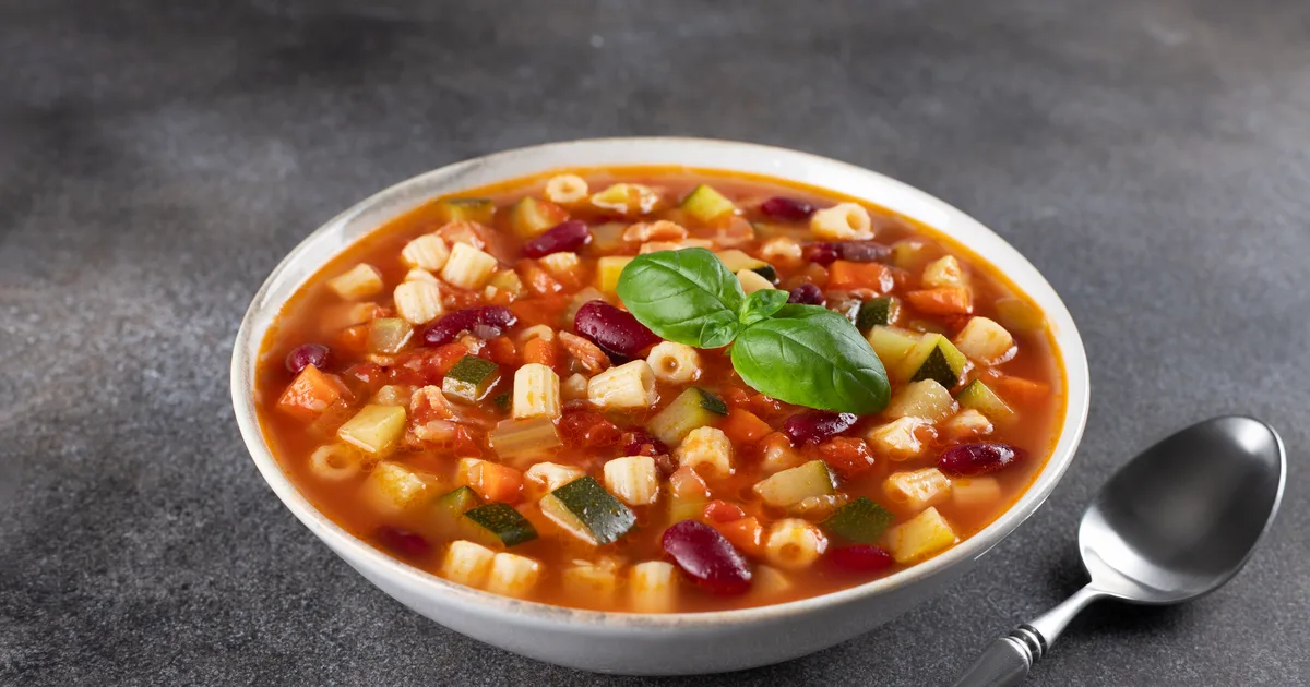 Minestrone w białej głębokiej misce z fasolą, makaronem, warzywami i tartym parmezanem